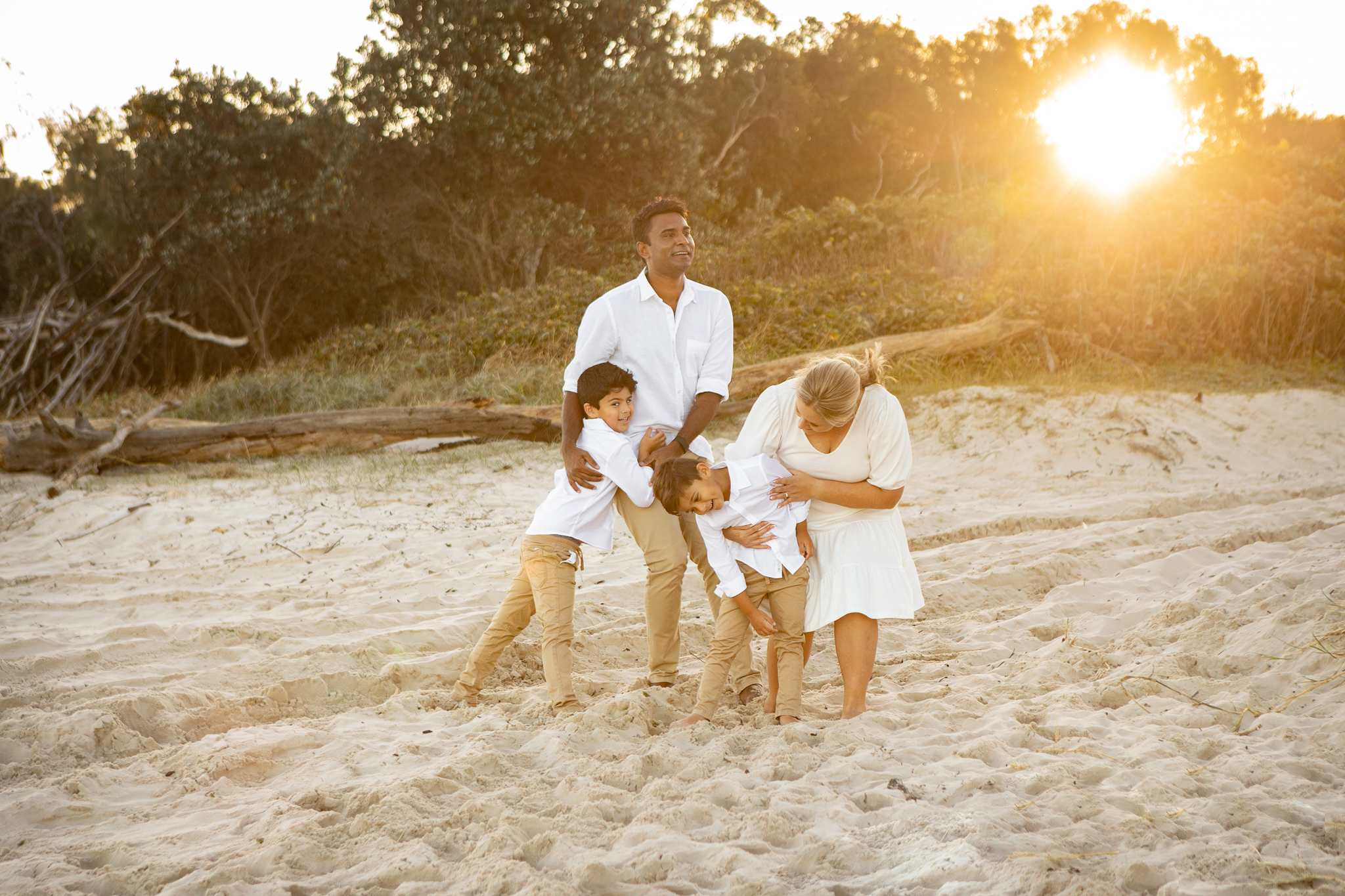 Family of four having a crazy, fun cuddle on the beach at sunset