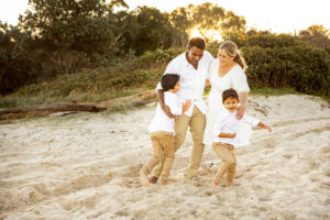 Family of four on the beach at sunset, one child running and smiling towards the camera