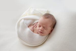 newborn baby curled up in white blanket