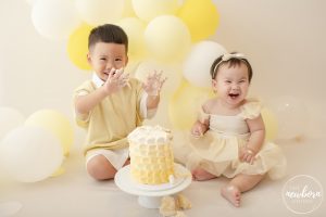 siblings enjoying a yellow and white themed cake smash
