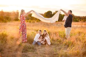 Beautiful and fun family moment with parents and children laughing together in a field during golden hour. Captured by The Newborn Studio, specialising in natural family photography.