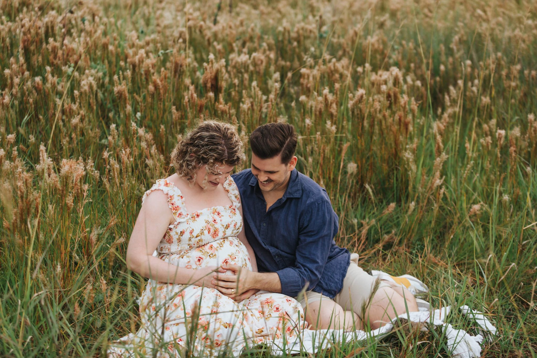 couple sitting in long grass with maternity session